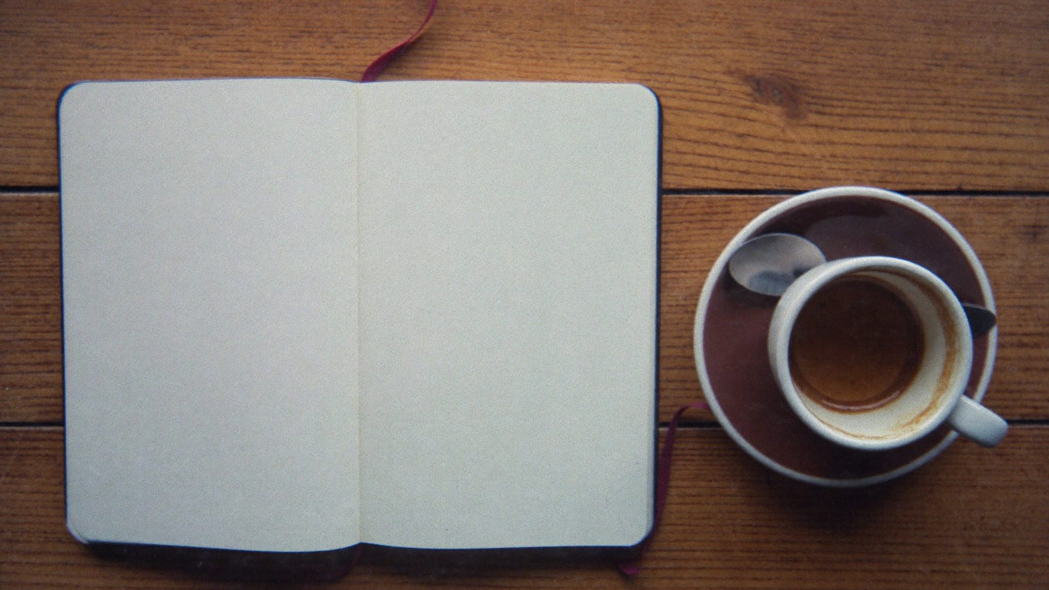 Caderno manuscrito com a ementa, ao lado de um café, sobre a mesa do Nyxenix